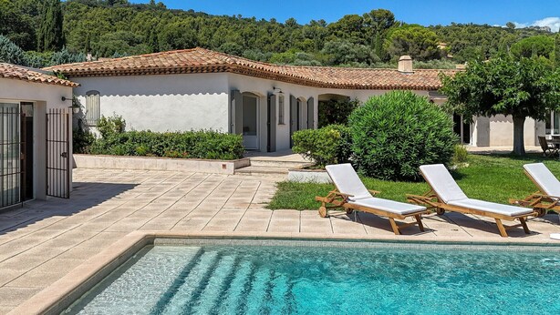 A pool area with lounge chairs, a tiled patio, and a building with a tiled roof.