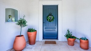 A front door with a blue door and a wreath, flanked by terracotta planters with green plants.