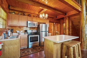 A wooden cabin kitchen with a central island, stainless steel appliances, and a chandelier.