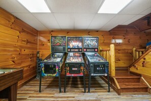 Una habitación con paredes de madera y techo inclinado, que cuenta con cuatro máquinas de pinball y una mesa de billar.