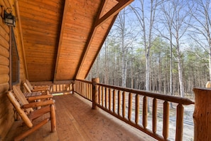 A wooden cabin with a balcony, log walls, and a view of a forest.