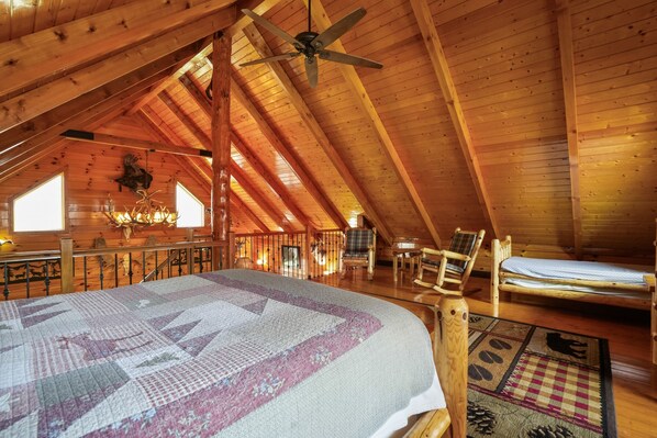 A cozy attic bedroom with a large bed, a ceiling fan, and a rustic wooden interior.