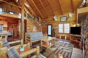 A spacious wooden cabin with a loft bedroom, a cozy living room with a sofa and coffee table, a fireplace, and a staircase leading to the upper level.