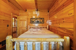 A wooden cabin interior with a bed, a door, and a wall-mounted picture.