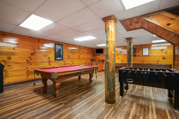 A wooden-floored room with a pool table and foosball table.