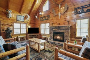 Interior de una cabaña de troncos con chimenea, mobiliario de madera y varios trofeos de animales.