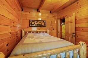 Un dormitorio de cabaña de madera con una cama, un colcha y un cuadro de animales salvajes en la pared.