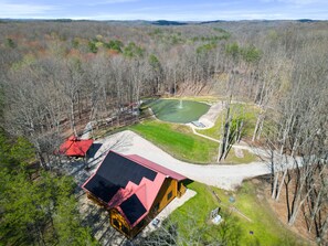 An aerial view of a lodge with a red-roofed cabin, a pond, and a surrounding forest.