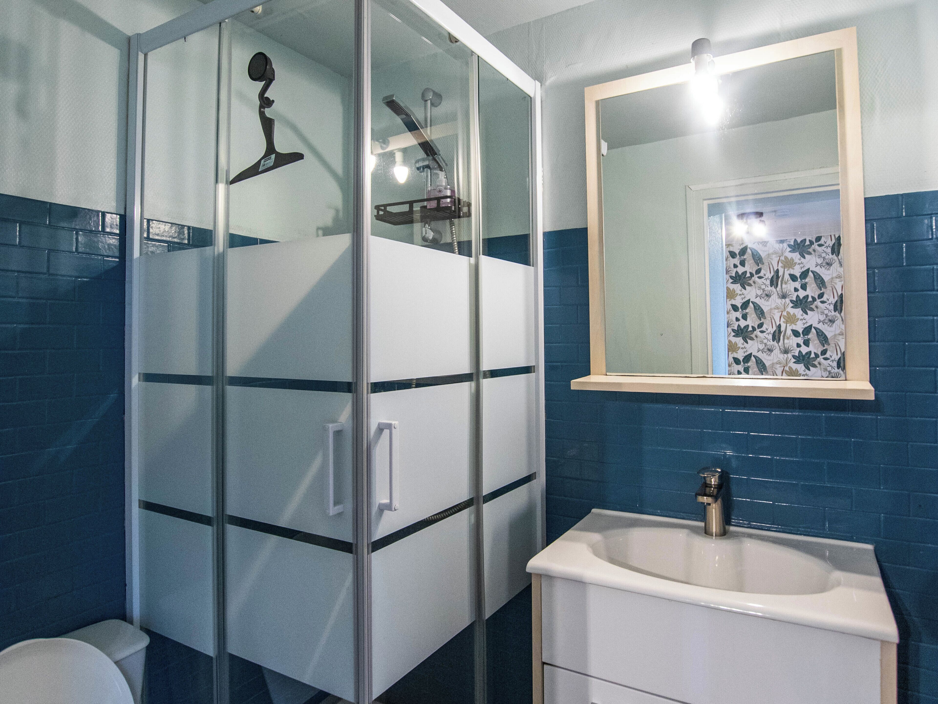 A bathroom with a glass shower enclosure, a white sink, and a mirror with a floral tile backsplash.