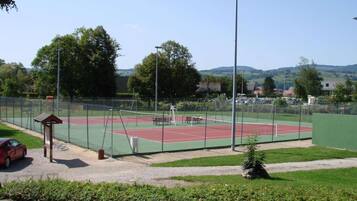 A tennis court with a fence, a small pavilion, and a car parked nearby.