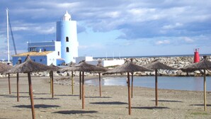Ένα παραθαλάσσιο κτίριο με έναν φάρο, σκεπαστές ομπρέλες από καλάμια και μια βραχώδη ακτογραμμή.