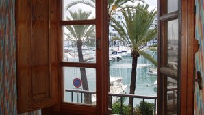 Ένα ξύλινο παράθυρο με θέα σε μια μαρίνα, φοίνικες και σκάφη.