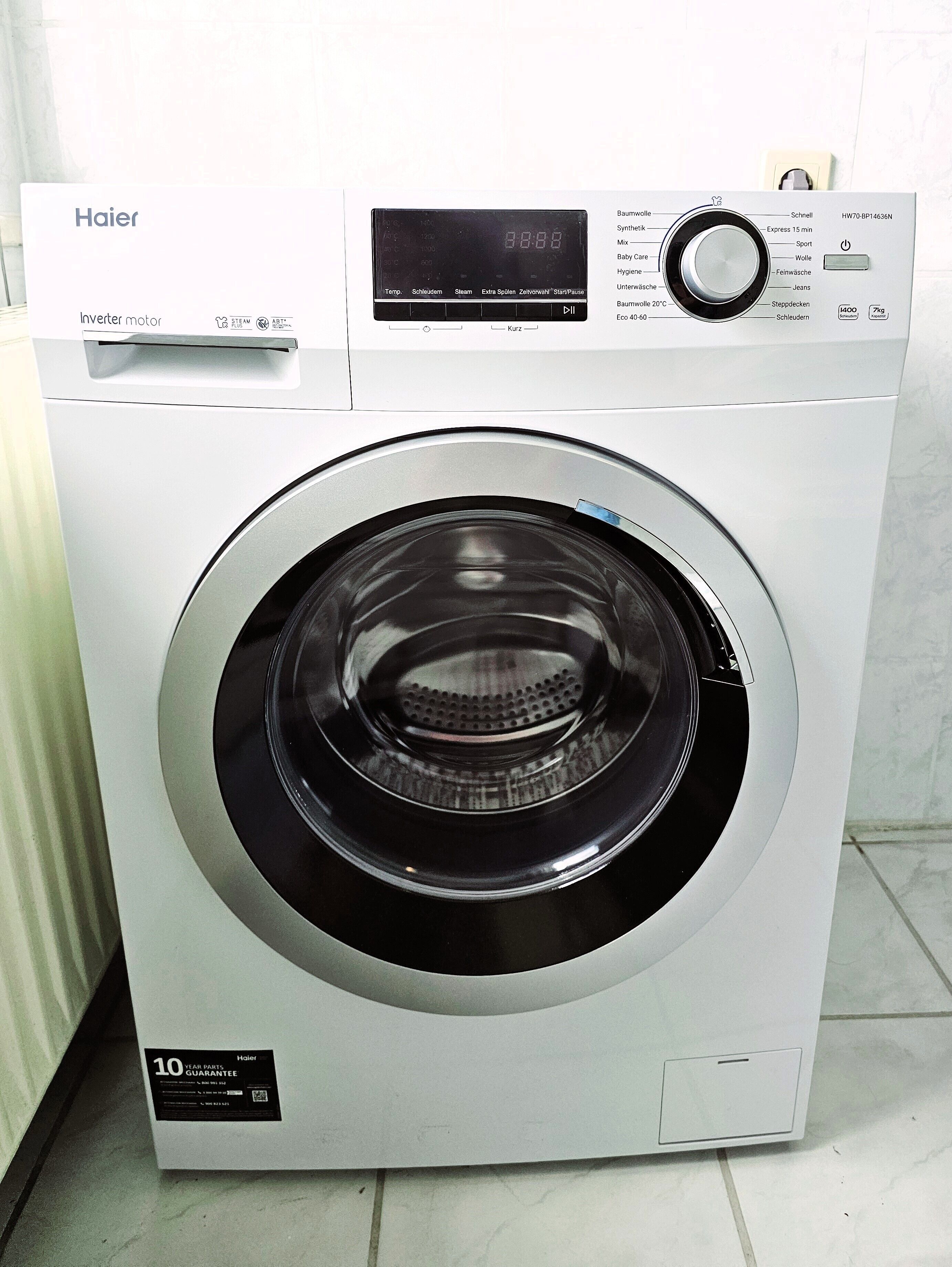 Eine Haier Waschmaschine mit Inverter-Motor, digitalem Display, Bedienfeld und einem Etikett für eine 10-jährige Teilegarantie.