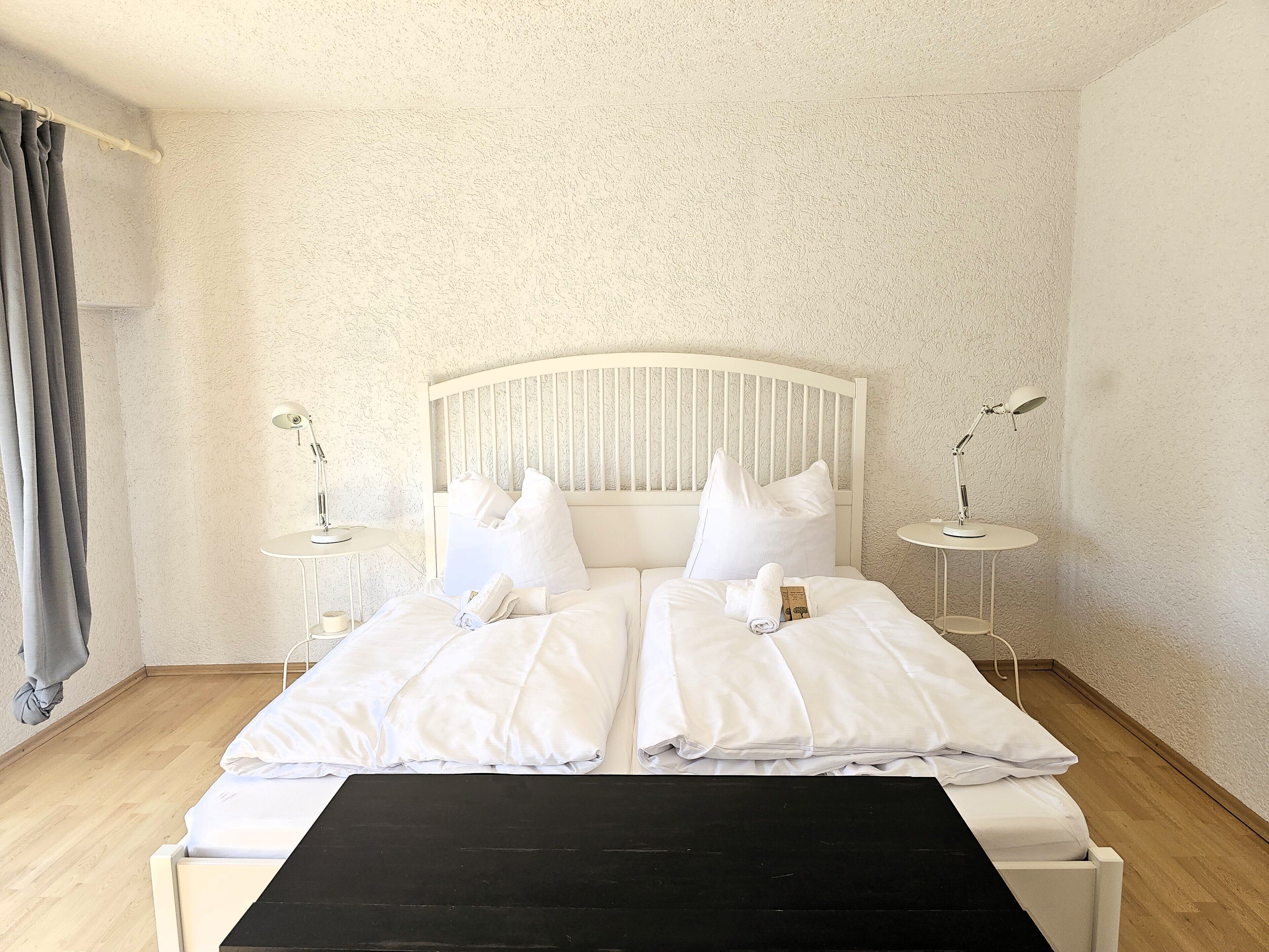 Un lit bien fait, avec du linge de lit blanc, deux tables de chevet avec des lampes et un plancher en bois.