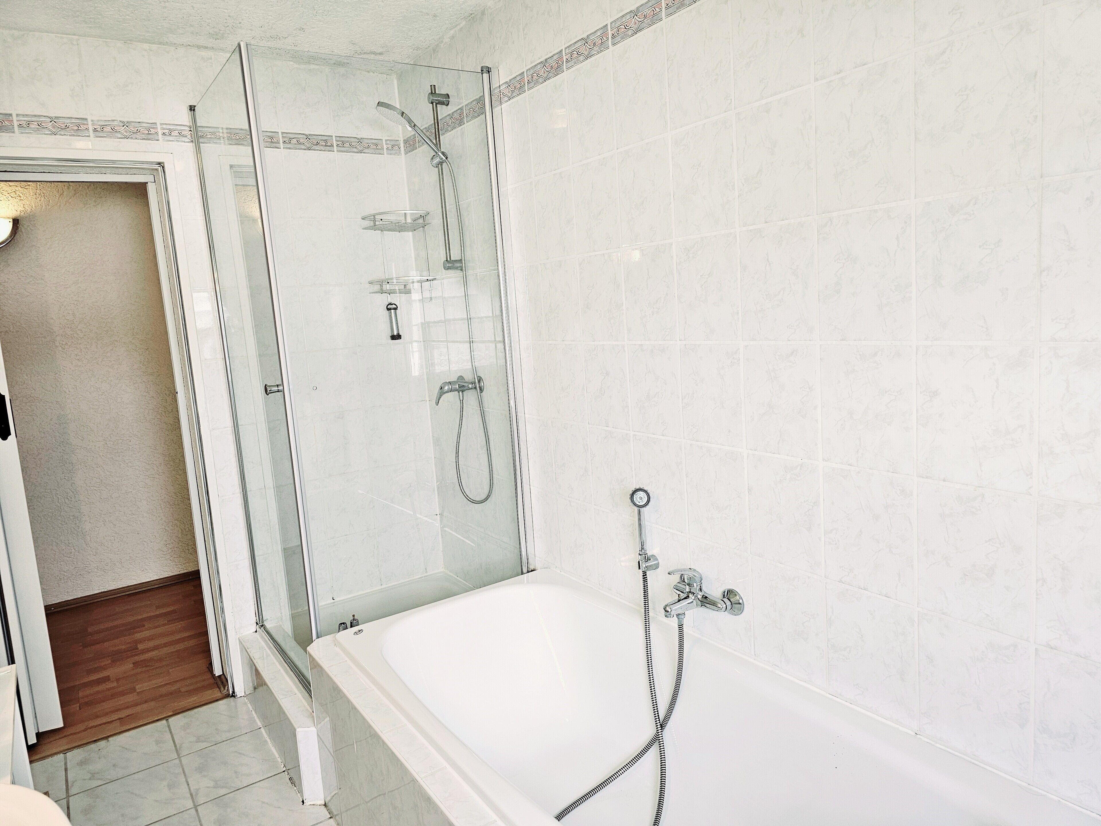 Ein Badezimmer mit einer Glaskabine zur Dusche, einer Badewanne und einem gefliesten Boden.