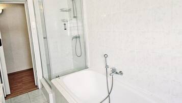 Ein Badezimmer mit einer Glaskabine zur Dusche, einer Badewanne und einem gefliesten Boden.