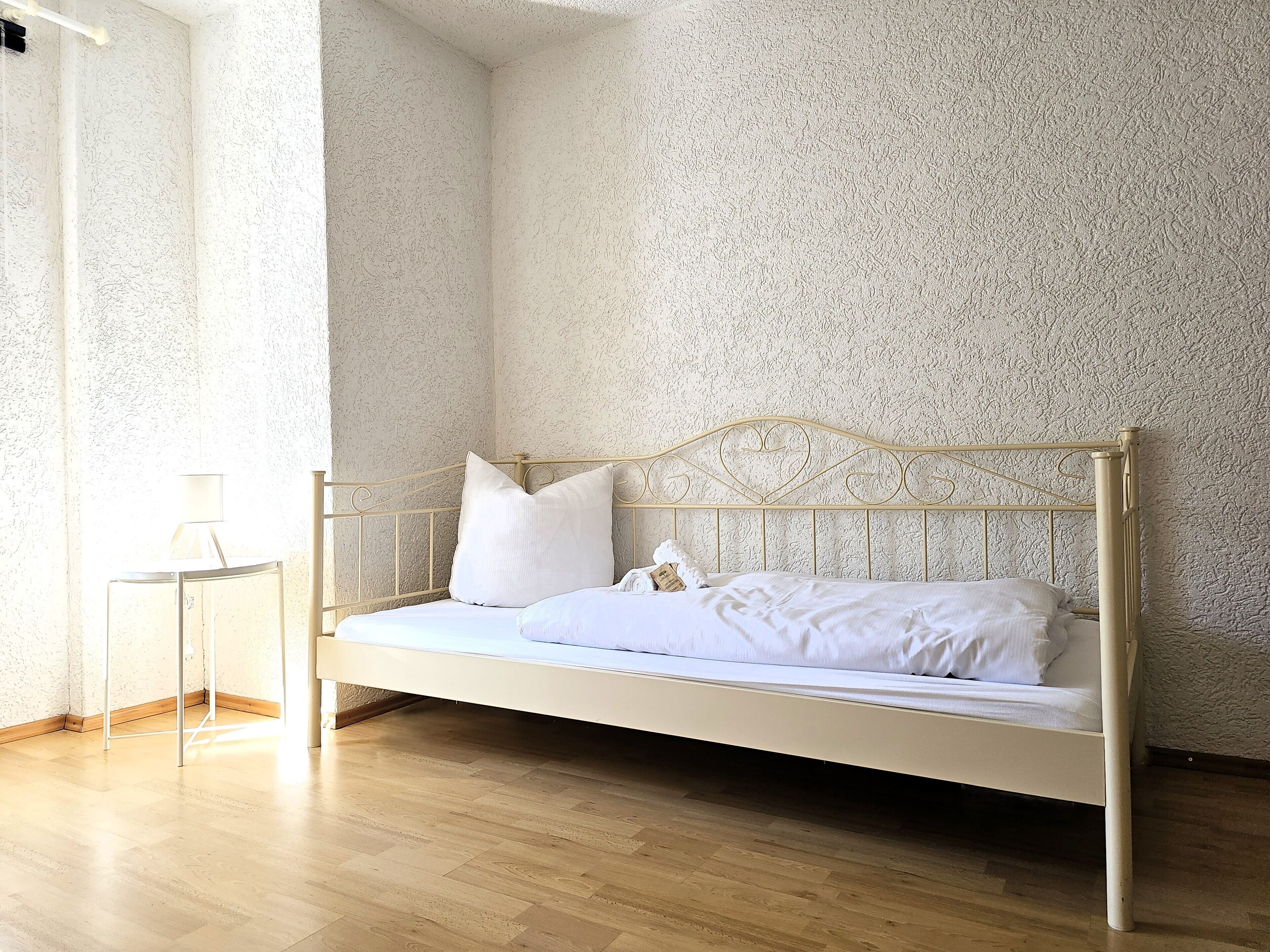 A single bed with a metal frame and white bedding in a room with textured walls and wooden flooring.