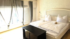 A bedroom with a bed, curtains, a bedside table, and a lamp. - Apartmenthaus - Mackenbach (Mackenbach)