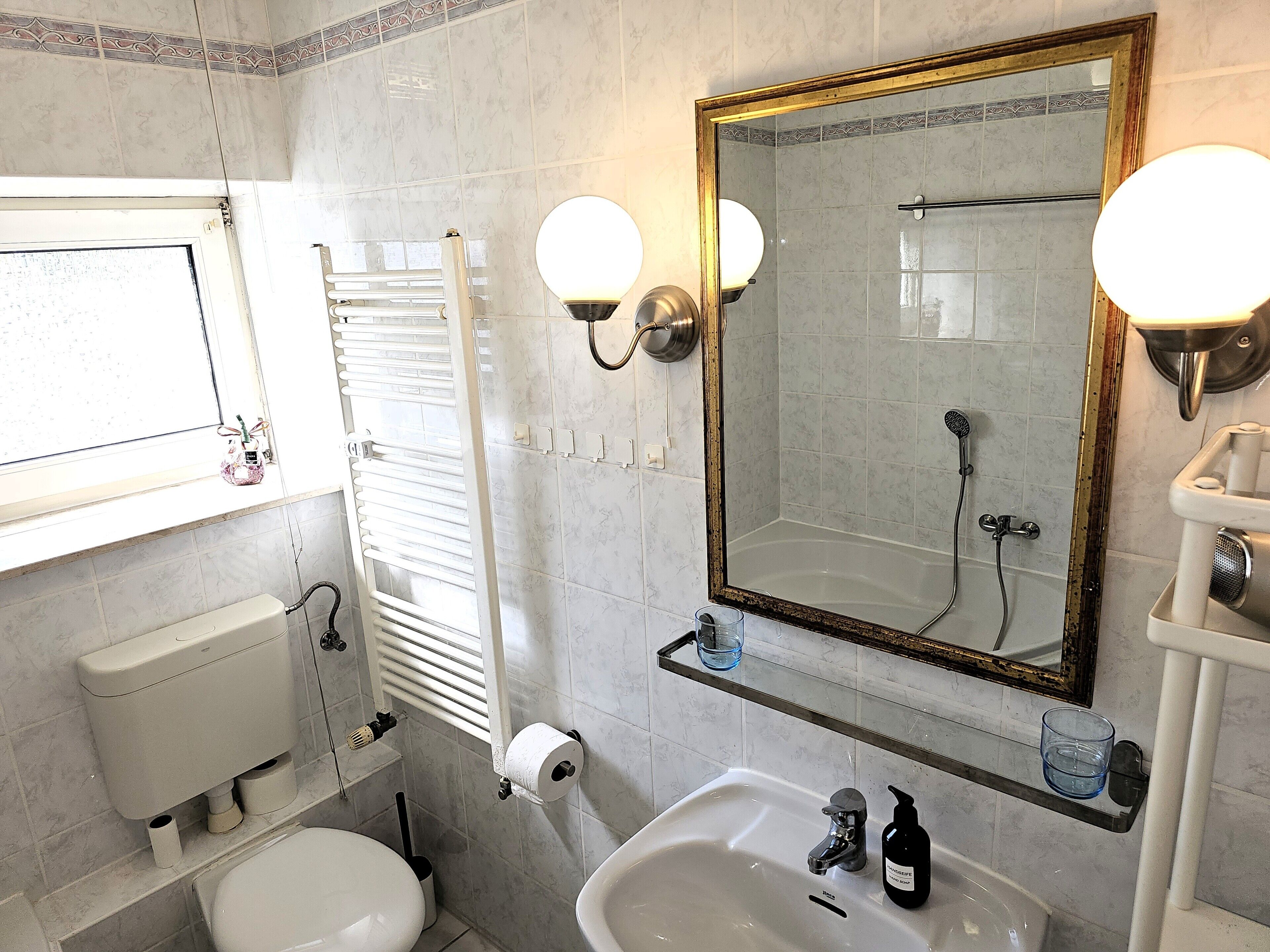 Et badeværelse med toilet, vask, spejl og bruser.
