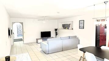 Un salon moderne avec un canapé gris, un téléviseur à écran plat et un coin repas comprenant une table et des chaises.