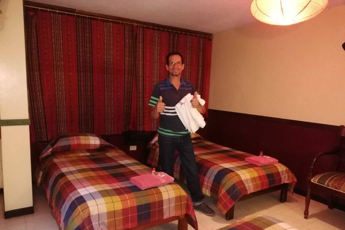 A hotel room with two single beds, each with a colorful plaid bedspread and a pink pillow.