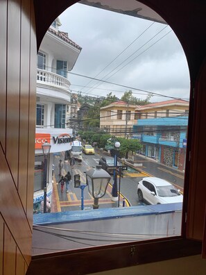 A view through a window of a street scene with buildings, a tram, and a white car. - Hostal Flying Donkey (Otavalo)