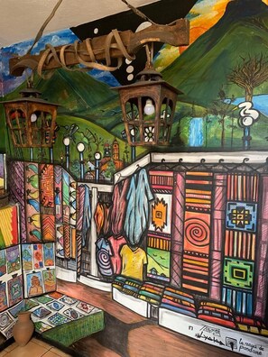 A colorful mural with a variety of patterns and designs, including a street scene with buildings and a mountain in the background. - Hostal Flying Donkey (Otavalo)