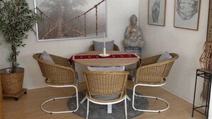 Un coin repas avec une table ronde, des chaises en osier, une statue de Bouddha et un grand tableau encadré.