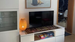 Un salon avec un téléviseur posé sur un meuble blanc, un tableau représentant une personne au bord de la mer et, en arrière-plan, un papier peint représentant une nuit étoilée.