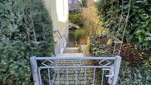 Une entrée fermée par un portail en métal et un chemin pavé de pierres menant à un bâtiment.