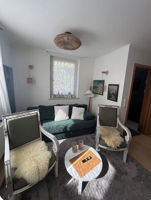A living room with a green sofa, two armchairs, a round coffee table, and a hanging light fixture.