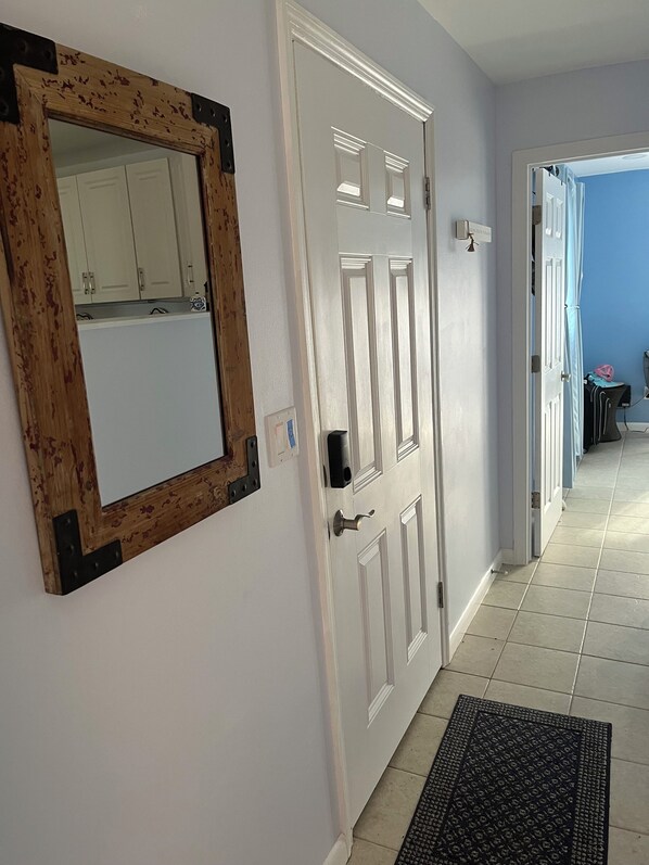 A hallway with a white door, a wooden-framed mirror, and a tiled floor. - Treasure Cay Beach Villa Magic (Treasure Cay)