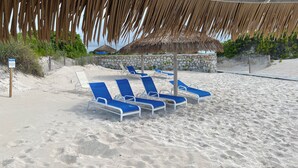 A beach with sun loungers under a thatched roof, a stone wall, and a sign that reads "THANK YOU". - Treasure Cay Beach Villa Magic (Treasure Cay)