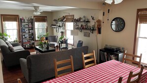 A cozy living room with a sofa, a dining table with a checkered tablecloth, and a bookshelf filled with various items. - Charming cul-de-sac 5BR 3.5BA in State College, PA (Port Matilda)