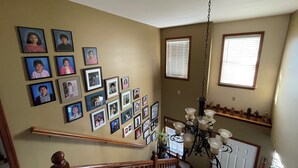 A staircase with a wooden handrail, a chandelier, and a wall adorned with framed photographs. - Charming cul-de-sac 5BR 3.5BA in State College, PA (Port Matilda)