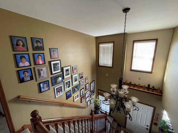 Un escalier avec une rampe en bois, un lustre et un mur décoré de photographies encadrées.