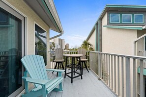 Un balcon avec deux fauteuils Adirondack et une petite table ronde, donnant sur une vue panoramique de la ville, avec des palmiers.