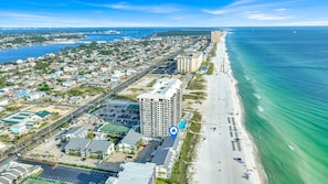 An aerial view of a coastal city with a beachfront, high-rise buildings, and a clear blue sky.