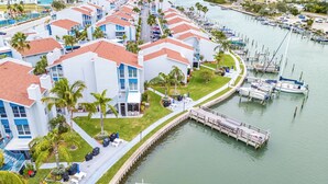 A marina with boats docked, a pedestrian walkway, and a building with a red roof and white walls. -  Charming 2-bedroom, 1.5-bath condo located on the intercoastal waterway (Madeira Beach)