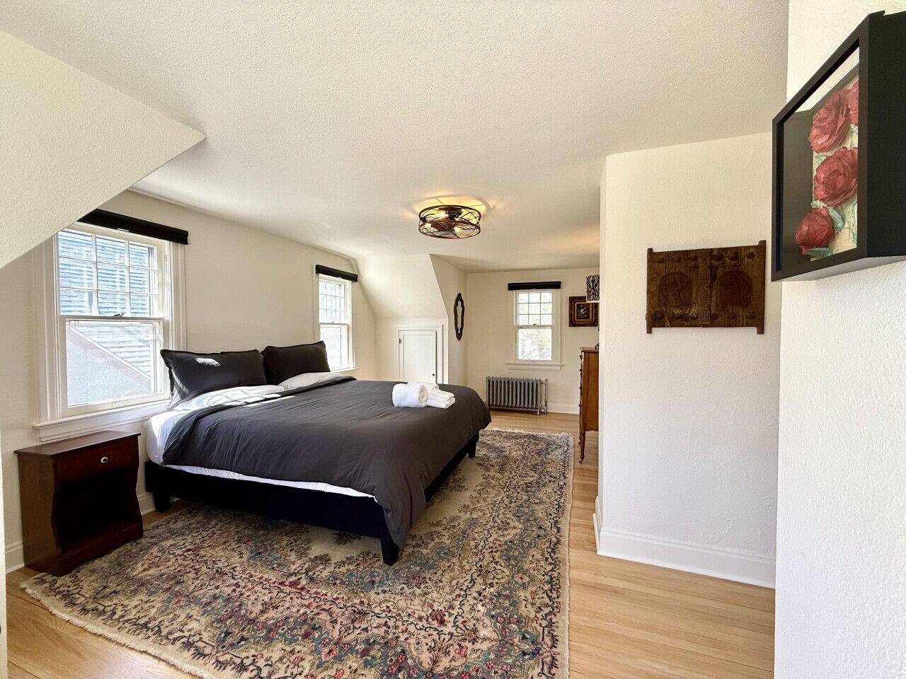 Une chambre à coucher avec un grand lit, une table de chevet en bois, une lampe sur pied et un tableau encadré au mur.
