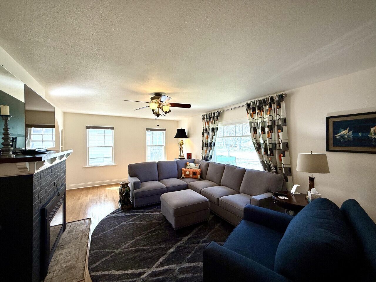 A living room with a sectional sofa, a ceiling fan, and a fireplace.
