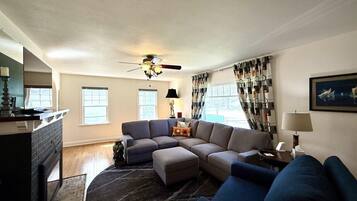 A living room with a sectional sofa, a ceiling fan, and a fireplace.