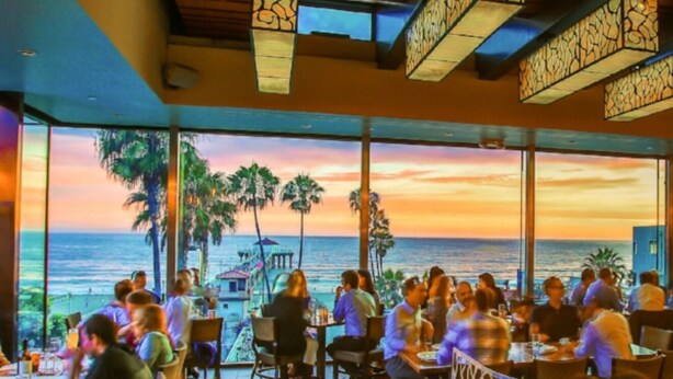 A restaurant with a view of the ocean at sunset, featuring large windows and wooden ceiling beams. - Coastal Charm Awaits: Book Your Getaway Today! (Manhattan Beach)