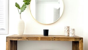 A wooden console table with a round mirror, a white vase with a plant, and two decorative candle holders. - Coastal Charm Awaits: Book Your Getaway Today! (Manhattan Beach)