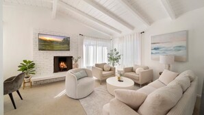 A modern living room with a fireplace, white furniture, and a large window. - Coastal Charm Awaits: Book Your Getaway Today! (Manhattan Beach)