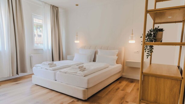 A modern hotel room with a large bed, wooden flooring, and a built-in wooden shelf.