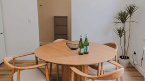 A round wooden dining table with four chairs, two bottles on the table, and a hanging light fixture.