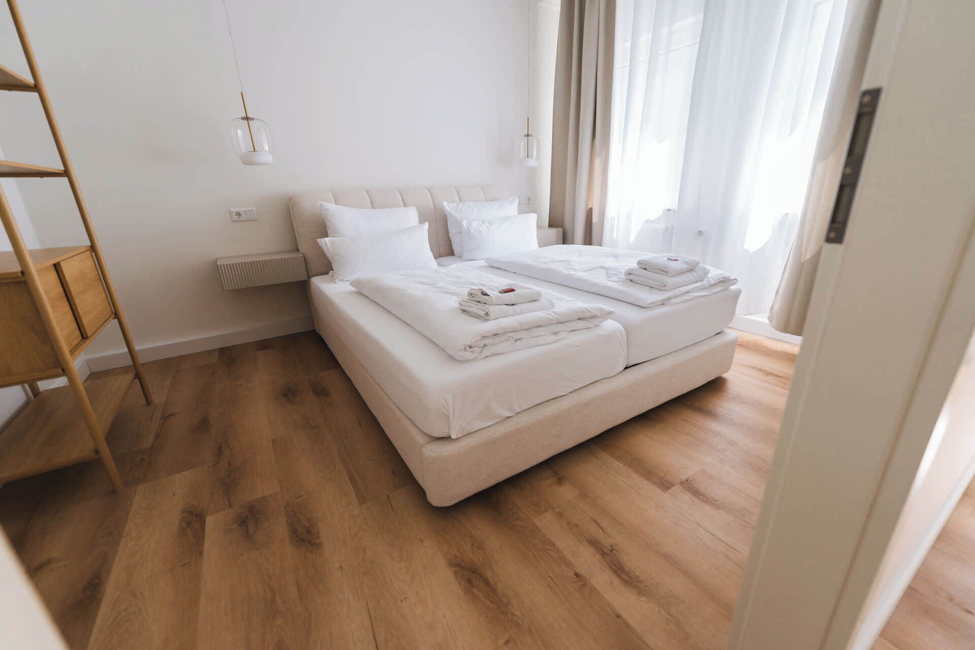 Un dormitorio moderno y minimalista con cama doble, suelo de madera y una mesita de noche tipo escalera.