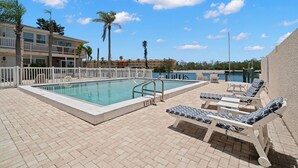 A swimming pool with lounge chairs and a view of a building with multiple floors and balconies. - Cozy Condo in Siesta key with boat dock (Sarasota)