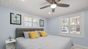 A bedroom with a bed, a nightstand, a ceiling fan, and two windows with shutters. - Cozy Condo in Siesta key with boat dock (Sarasota)